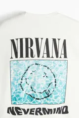 Remera color crema de corte holgado con estampado frontal del logo de la banda Nirvana y el título de su álbum Nevermind en color negro.