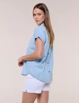 Blusa de diseño recto y textura suave de denim liviano color celeste, con cuello solapa abierto en V, pechera con detalle pespunteado y pliegue central. Presenta mangas cortas caídas con dobladillo fijo y ruedo ligeramente curvo.