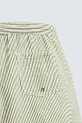 Bañador de hombre color verde claro con finas rayas blancas verticales (efecto seersucker). Tiene cintura elástica ajustable con cordón verde, bolsillos laterales y un bolsillo trasero de vivo.