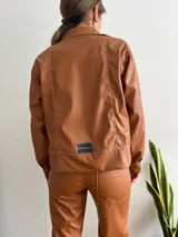 Campera marrón de cuero sintético con cierre frontal, cuello camisero y costuras decorativas en hilo blanco.