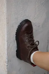 Borcegos de cuero charolado negro con cordones jaspeados en tonos marrones y suela track dentada con costura blanca visible.