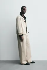 Sobrecamisa de hombre color beige claro, con cuello de solapas de pico, manga larga y cierre frontal de botonadura. Presenta bolsillos de vivo en la cadera.