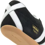 Championes Adidas modelo Tokyo, de diseño clásico y perfil bajo. Confeccionados en gamuza negra con las icónicas tres bandas laterales en cuero blanco y suela de goma color caramelo. Presenta el logo de la marca y el nombre del modelo en dorado en el lateral.