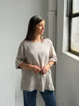 Blusa de lino color beige, de corte holgado, cuello redondo y mangas 3/4 con presillas y botones para sujetar el largo.