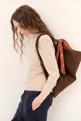 Sweater de punto color beige, de cuello redondo y manga larga, con detalle de pequeño bordado en el pecho.