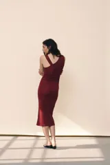Vestido midi color vino tinto, sin mangas, con escote drapeado tipo cascada y un detalle de argolla metálica plateada en el bretel derecho. Presenta frunces laterales a lo largo del torso.