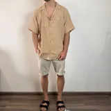 Camisa de manga corta confeccionada en muselina de textura arrugada, con cuello solapa, cierre frontal de botones y pequeño bordado en el pecho.