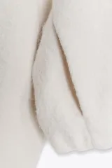 Chaqueta de textura bouclé en color crudo, con cuello subido, cierre frontal con cremallera, manga larga y puños elásticos.