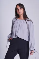 Blusa de manga larga color gris, con cuello redondo y diseño fruncido en el escote. Presenta mangas con puños elásticos y detalle de lazos ajustables.
