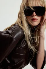 Chaqueta de efecto piel con cuello solapa, manga corta y cintura elástica. Presenta cierre frontal con cremallera y bolsillos decorativos en el frente.