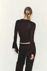 Camiseta de cuello redondo y manga larga, confeccionada en tejido rib con mezcla de lyocell. Presenta un diseño ajustado con terminación de volantes en los puños y bajo recto.