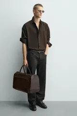 Bolso de viaje marrón con textura grabada, cierre de cremallera, bolsillo interior con cremallera, bolsillo frontal con cremallera, doble asa de mano y asa de hombro ajustable y extraíble.