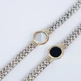 Pulsera de cadena tejida en plata con detalle central circular en oro que enmarca una piedra ónix negra.