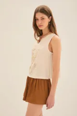 Musculosa color crema con estampado de mariposa y manos en dorado, escote en V con tachas y corte holgado.