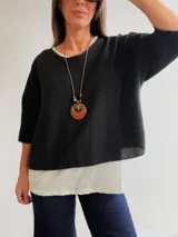 Conjunto de dos piezas compuesto por una remera básica de algodón blanca y un buzo negro de textura plisada con mangas murciélago. El buzo presenta detalles de hilo plateado en los bordes y un calce holgado. Incluye un collar largo con dije de madera y metal.