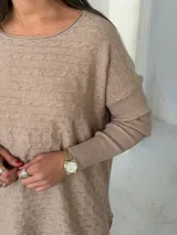 Sweater de punto color visón con diseño de trenzas horizontales, cuello redondo y mangas largas con puños acanalados.