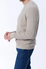 Buzo de punto en color taupe, con cuello redondo y textura acanalada. Presenta mangas largas y puños ajustados, ofreciendo un diseño clásico y versátil.