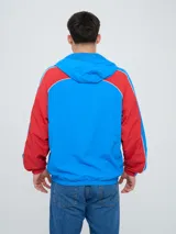 Campera deportiva Umbro del Club Nacional de Football, modelo Venti, para hombre. Diseño en color blanco con mangas azules y detalles de líneas rojas. Cuenta con capucha con cordón ajustable, cierre frontal y bolsillos. Presenta el logo de Umbro y el escudo del club bordados en el pecho.
