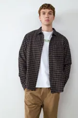 Camisa de manga larga confeccionada en franela con estampado a cuadros en tonos oscuros. Presenta cuello clásico, cierre frontal con botones, puños abotonados y un bolsillo aplicado en el pecho.