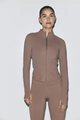 Campera deportiva de corte ajustado, color marrón tostado, con cuello elevado, cierre frontal completo, mangas raglán con abertura para el pulgar y bolsillos laterales con cierre.