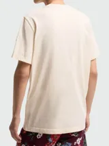 Remera de algodón color beige con cuello redondo, manga corta y bordado con la inscripción "Moncler Archive" en el pecho. Presenta un parche con el logo de la marca en la manga izquierda.