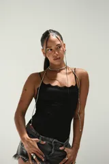 Collar tipo choker y tiras colgantes, compuesto por pequeñas cuentas plateadas. El diseño incluye un choker ajustado al cuello y dos tiras largas que caen sobre el pecho y los hombros, sujetas a una prenda negra con un broche metálico central.