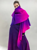 Prenda de abrigo tipo capa o chal de lana merino afieltrada, con diseño desestructurado y efecto degradé en tonos violeta y fucsia. Se ajusta al cuerpo mediante un nudo frontal.