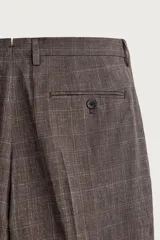 Pantalón de traje regular fit marrón con sutil estampado a cuadros, confeccionado en mezcla de lino y lana. Cuenta con bolsillos delanteros, bolsillos traseros de doble vivo con botón y raya marcada en el centro de las piernas.