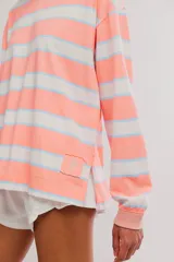 Remera manga larga de algodón con diseño de rayas horizontales en tonos verdes, azul marino, rosado y celeste. Presenta cuello redondo y un pequeño parche decorativo en el borde inferior.