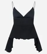 Top negro de breteles finos, con escote en V profundo y frunce bajo el busto. Presenta un corte peplum con volados asimétricos y bordes ondulados en la parte inferior y en las mangas largas que caen a los costados. La tela tiene una textura acanalada o plisada.