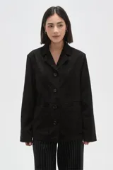 Chaqueta de gamuza sintética color negro, con cuello solapa, cierre frontal de botones y bolsillos delanteros aplicados. Presenta un corte holgado y mangas largas.