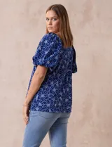 Blusa azul con estampado floral blanco, cuello cuadrado, mangas cortas abullonadas y frunce en los hombros.