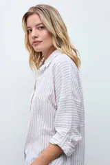 Camisa de corte holgado con diseño de rayas verticales en tonos beige y blanco, con sutiles destellos brillantes. Presenta cuello clásico, cierre frontal con botones y mangas largas con puños ajustables.