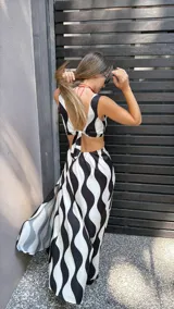 Vestido largo de tela sedosa con estampado de ondas verticales en blanco y negro, escote en V, cut out en la cintura, espalda regulable con lazo y elástico, y tajos laterales.
