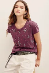 Remera de algodón color morado, con mangas cortas, cuello redondo y bordado de cuentas y pedrería en la parte frontal.