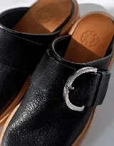 Mules de cuero negro con hebilla plateada y suela color madera.