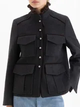 Chaqueta de paño gris con cuello mao y cuello desmontable con volados de gasa y puntilla. Presenta cierre frontal con botones metálicos, cuatro bolsillos delanteros con solapa y vivos en satén color chocolate que recorren el diseño.