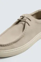 Zapato casual de hombre, color beige claro, con capellada de serraje (gamuza) y cordones finos. Presenta un detalle de bordón en el empeine y suela gruesa de goma a contraste en color crema.