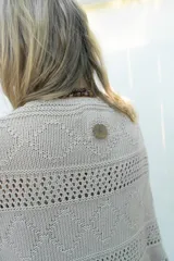 Poncho de tejido de algodón color beige claro, con diseño de punto calado y flecos en el borde inferior.