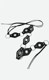 Cinto de cuero negro con diseño de piezas circulares unidas por argollas metálicas, decorado con tachas plateadas y tiras largas de cuero colgantes en el lateral.