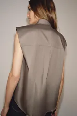 Camisa sin mangas confeccionada en algodón, con cuello redondo y detalle de lazada frontal. Presenta cierre frontal con botones ocultos por solapa y bajo redondeado.