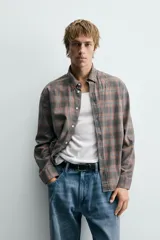 Camisa de corte relajado confeccionada en algodón, con estampado de cuadros en tonos marrones y grises. Presenta cuello abotonado, cierre frontal de botones y mangas largas con puños abotonados.