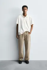 Remera polo color blanco roto, con cuello solapa, cierre frontal de tres botones y manga corta. Presenta un efecto lavado y corte regular fit.