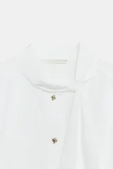 Camisa de algodón color blanco, con cuello subido y detalle de pañuelo incorporado, manga larga con puños anchos y cierre frontal con botones joya dorados.