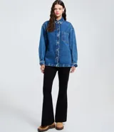 Camisa de corte oversized confeccionada en denim de algodón con lavado gris desgastado. Presenta cuello clásico, cierre frontal con botones metálicos, manga larga con puños abotonados y un bolsillo aplicado en el pecho. El diseño incluye un bajo redondeado.