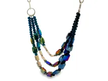 Colgante de tres hilos con cuentas de cristal facetado en tonos iridiscentes, azules y verdes, con detalles metálicos plateados.