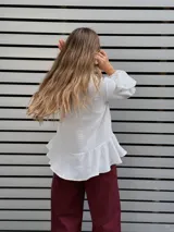 Blusa blanca de textura arrugada, con escote en V y lazos para anudar. Presenta mangas largas con puños acampanados y un diseño con volado en el ruedo.