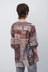 Camisa de corte recto con cuello mao y cierre frontal parcial de botones. Presenta un diseño estampado tipo patchwork con motivos florales y geométricos en tonos tierra, marrones y beige. Posee mangas tres cuartos con puños simples.