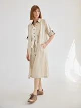 Vestido camisero midi de lino color beige, con diseño de manga corta con solapa, cuello camisero, bolsillo trasero con solapa y botón, y aberturas laterales en el ruedo.