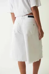 Bermuda de denim blanco de tiro bajo y corte holgado, con detalles desgastados y terminación desflecada en las perneras. Cuenta con trabillas en la cintura y cierre frontal con botón y cremallera.